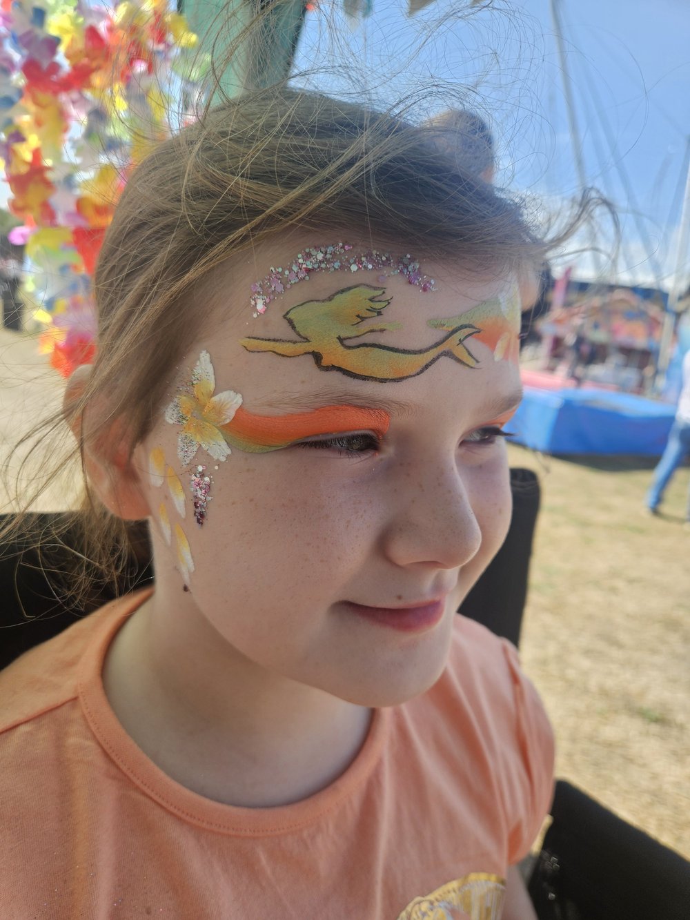 Orange and yellow mermaid face painting with flowers and glitter